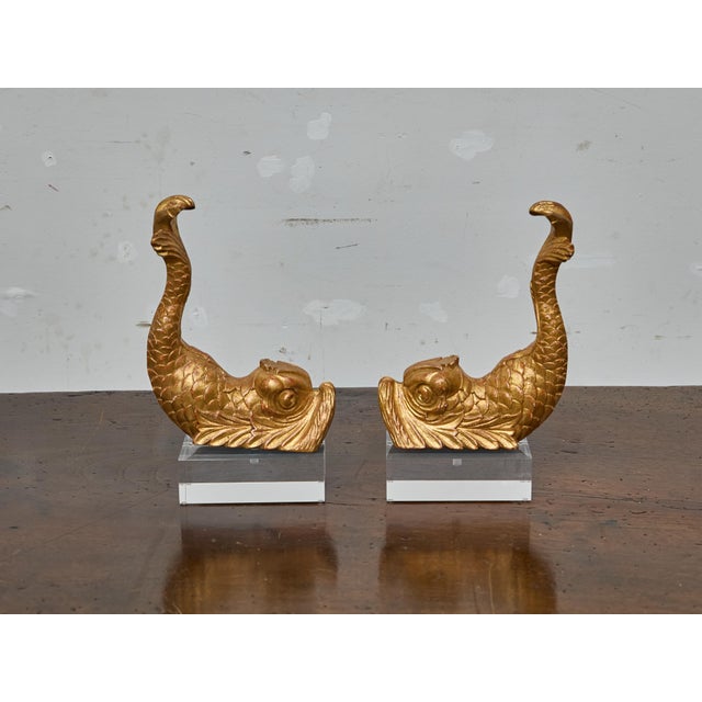 This striking pair of carved giltwood dolphin figures mounted on clear lucite bases likely began their life as decorative...