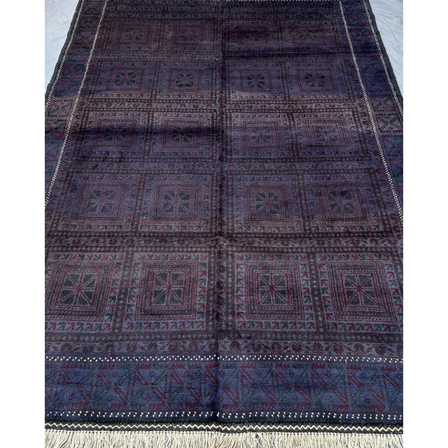 This hand-knotted Afghan Baluch rug lives entirely in the dark end of the spectrum — deep midnight indigo, plum, dusty...