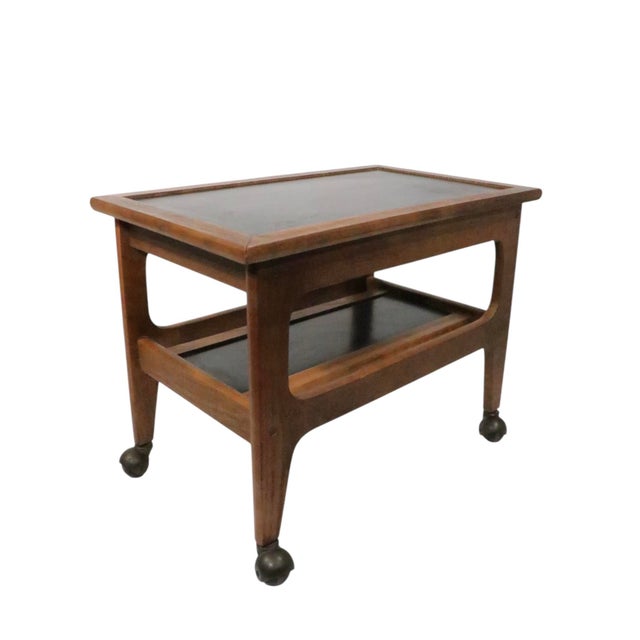 Classic mid century side table, rolling cart having black laminate surfaces within a sculptural solid wood frame, on...