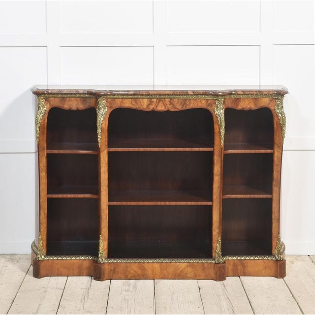 19th century figured walnut cross banded open bookcase, of Louis XV design. The breakfront top having a moulded edge, over...