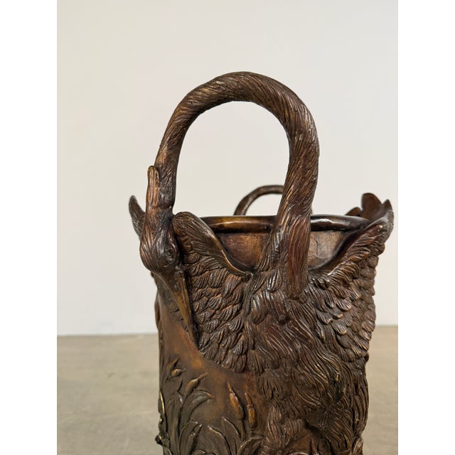 A beautifully sculptural bronze vessel featuring a pair of elegant cranes forming the handles, set against a richly...