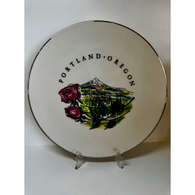 This illustrated decorative plate celebrates Portland, Oregon, featuring pink roses in the foreground, a stylized...