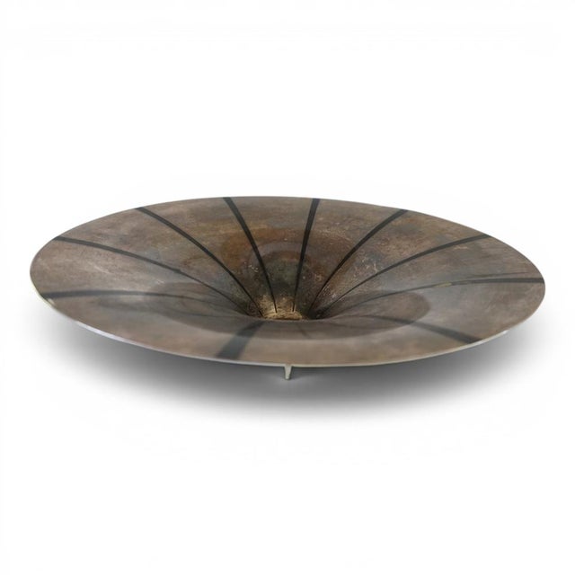 This silver-plated, sculptural brass bowl, with its conical shape and dark rays radiating from the center, exudes absolute...