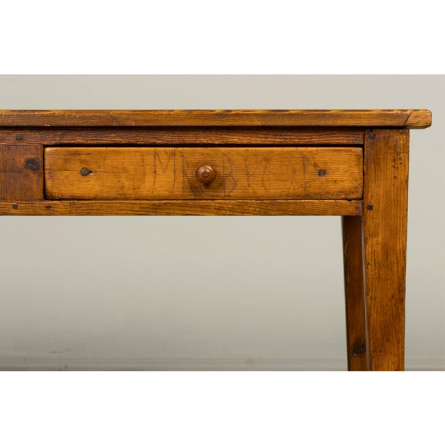 A late 19th-century French rustic farmhouse writing table crafted from solid pine, sourced in Provence, France. The table...