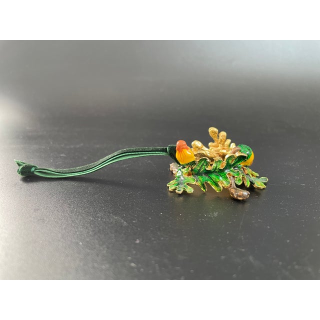 A metal ornament in the form of a wreath of oak leaves and acorns, crafted in gold-tone metal with colorful enamel...