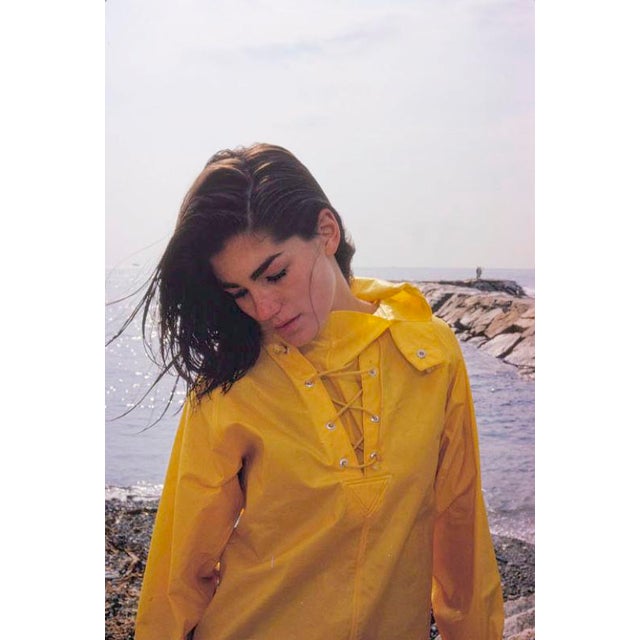 Minnie Cushing In Yellow by Toni Frissell Model Minnie Cushing wearing a yellow waterproof jacket stands by the ocean,...