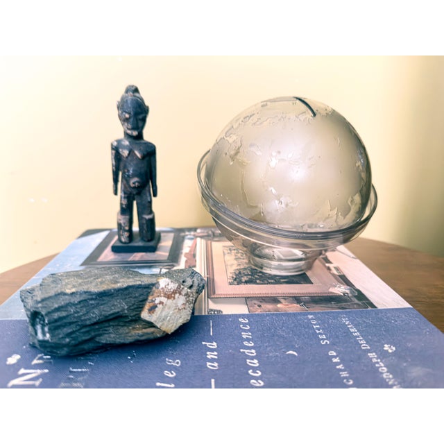 A collectible globe money box in smoky resin, with embossed continents and a coin slot at the top. The globe rests on a...