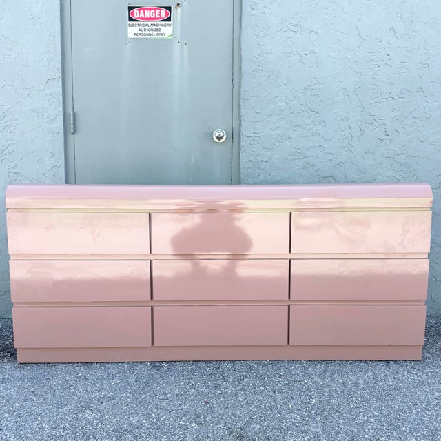 A striking postmodern waterfall dresser finished in a soft blush pink high-gloss laminate, showcasing sleek lines and...