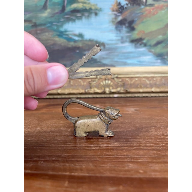 This charming antique brass toned figural lock takes the form of a small dog wearing a collar and scarf, cleverly...