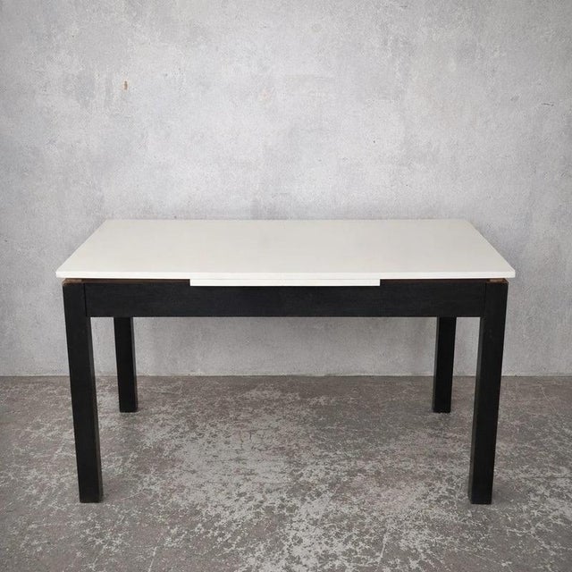 A stylish mid-century modern extending dining table, combining a crisp white Formica top with a contrasting dark stained...