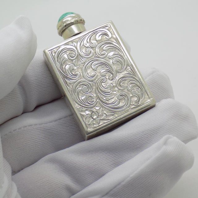 This vintage silver beauty accessory depicts a chiseled scent flask topped with a turquoise colored semi precious stone...