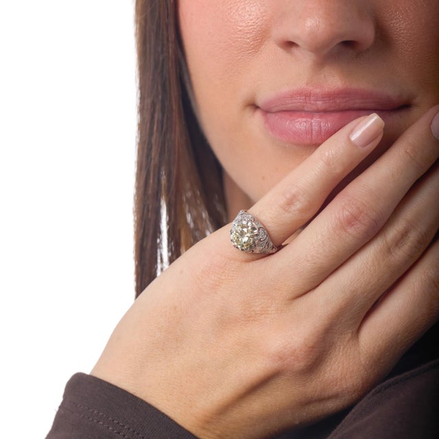 This Art Deco platinum engagement ring showcases a striking round brilliant diamond whose warm antique hue and bold...