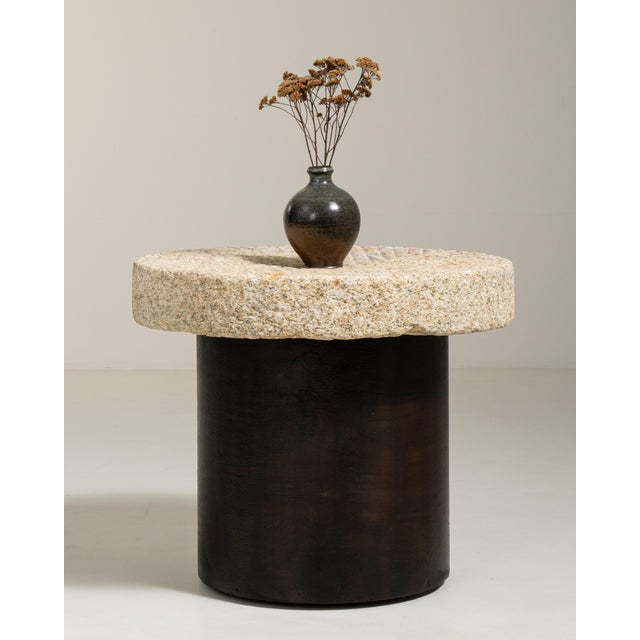 A compact side table combining a heavy stone top with a simple iron cylindrical base, reflecting a blend of utilitarian...