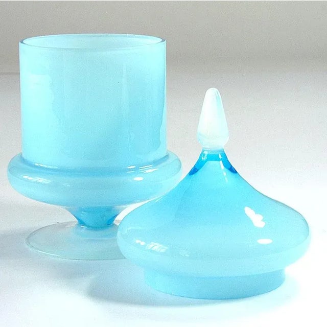 A decorative container made of glass -colored glass in a delicate, blue color. The foot and cover of the cover are also...