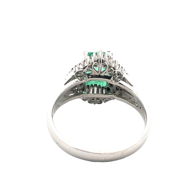 Striking platinum ring featuring a vivid emerald-cut emerald at the center, framed by a radiant halo of baguette and round...