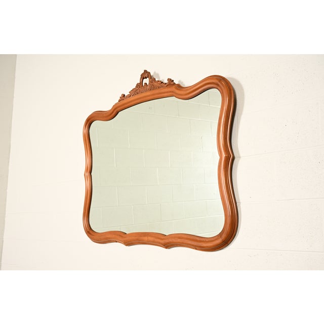 A gorgeous French Provincial Louis XV style carved fruitwood framed wall mirror In the manner of Romweber USA, 1950s...
