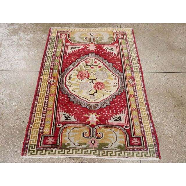 A vintage Turkish Ghiordes throw rug. A lopsided oval old ivory medallion contains a four rose and stem device, on a red...