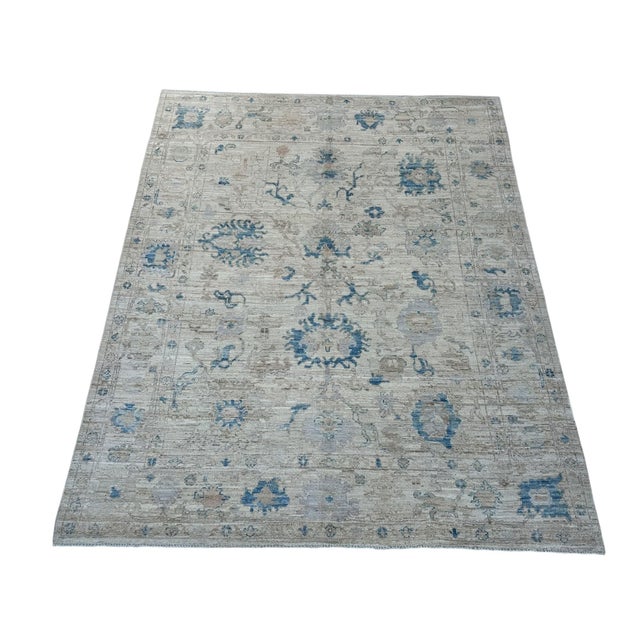 Light blue floral medallions and delicate scrolling vines decorate the cream field of this handmade Oushak wool rug....