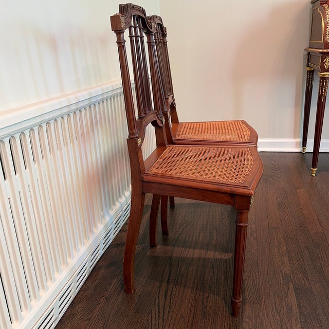 An exquisite pair of French antique petite caned seat side chairs constructed of solid wood with elegant bronze accents,...