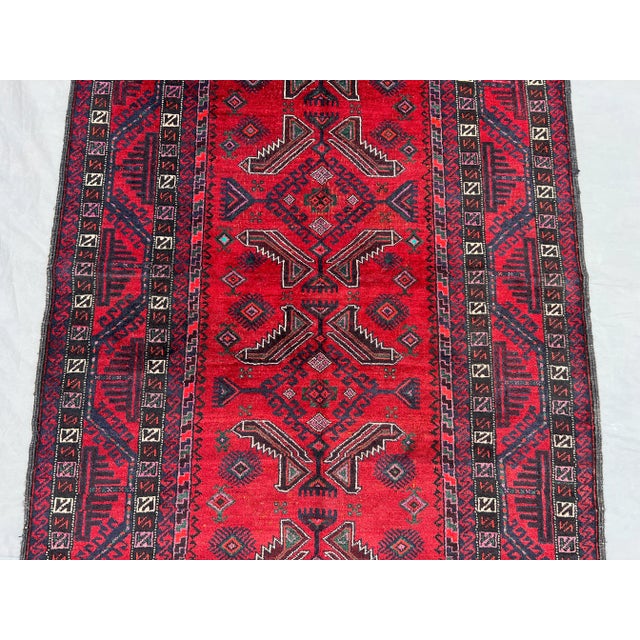 This beautiful vintage Afghan Baluchi rug features a striking red field with tribal geometric patterns in shades of navy,...