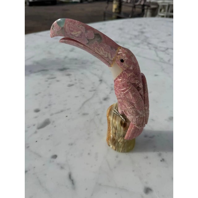 This sculpture is carved of pink quartz toucan. It depicts a parrot perched on a tree stump carved from onyx.