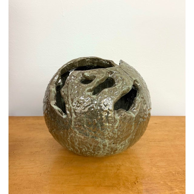 A sculptural ceramic vessel featuring a rounded form with irregular openings and a richly textured surface. Glossy glaze...