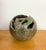 A sculptural ceramic vessel featuring a rounded form with irregular openings and a richly textured surface. Glossy glaze...