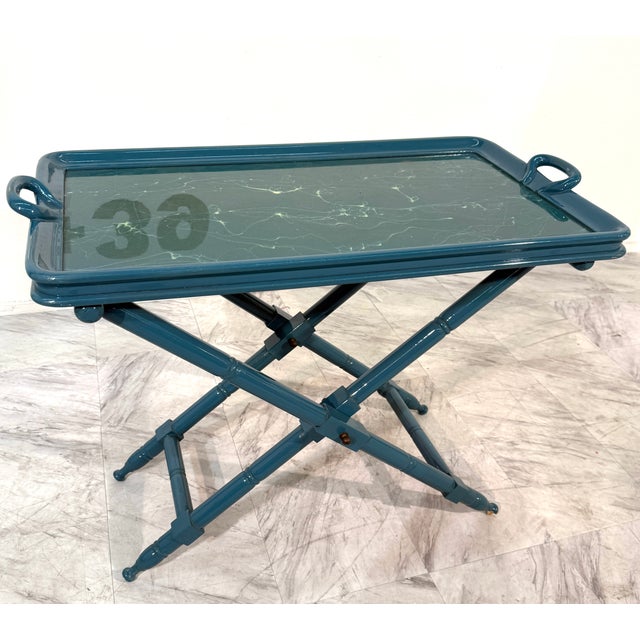 Elegant vintage folding tray table, handcrafted in Italy. The piece features a lacquered wooden frame in a rich teal...