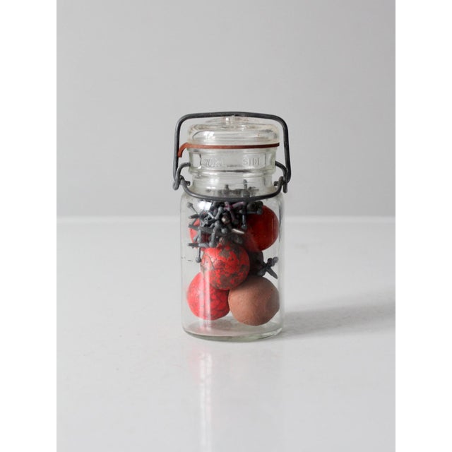 A vintage mid-century set of jacks and balls presented in a clear bail-lid glass jar. The cast-metal jacks and softly worn...