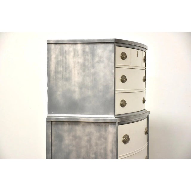 A painted white, metallic, and grey tall dresser. Minor wear on paint with age and use. 36” wide. 19” deep. 53” tall.