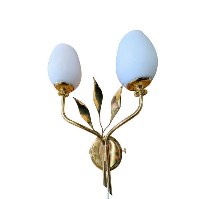 The brass frame of the itsu ey 5700 wall lamp resembles a branch, decorated with three graceful, leaf-like elements. Two...