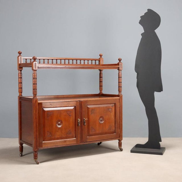 Walnut-stained oak sideboard. Base with a pair of carved paneled doors, upper part with a shelf supported by four turned...