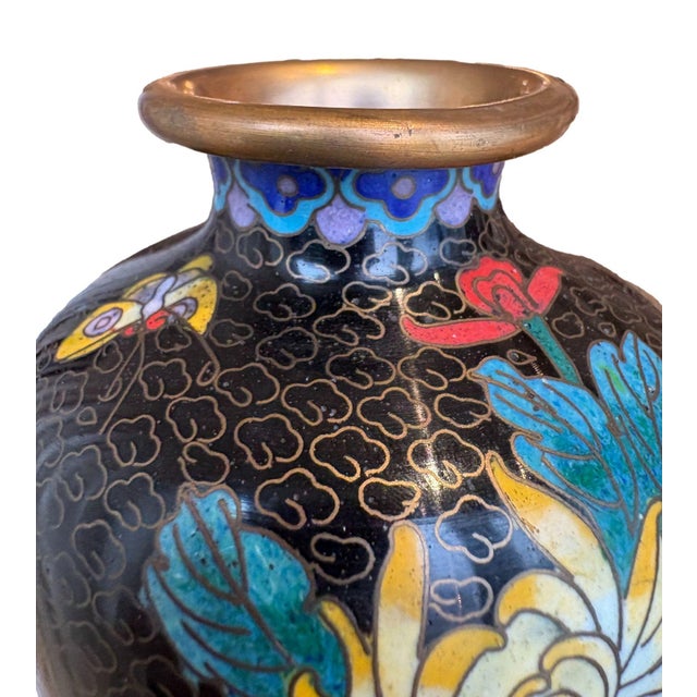 This small cloisonné vase features a black background adorned with intricate gold wire cloud motifs, framing bright floral...