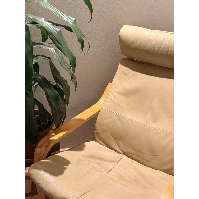 Iconic ikea poäng lounge chair dating from 2005, featuring a warm natural wood frame and a beautifully aged cream leather...