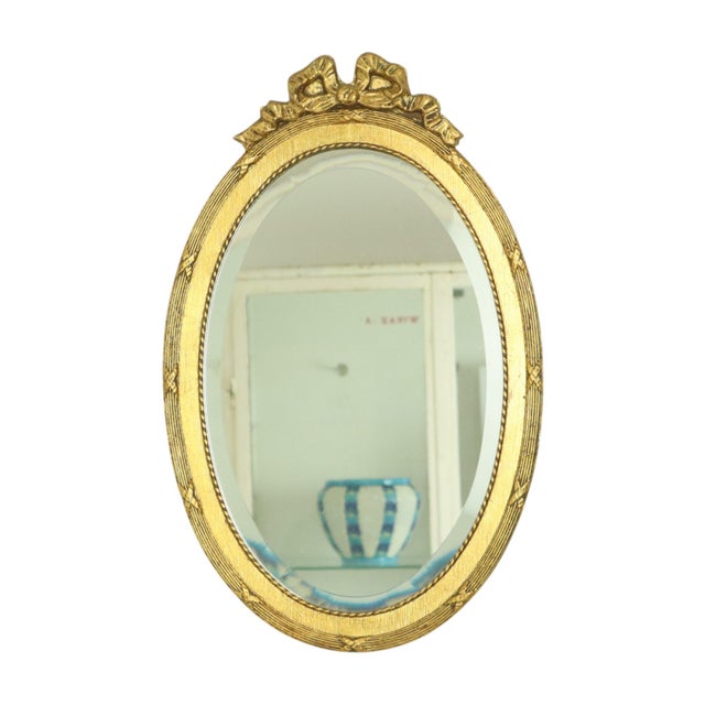 French oval gold mirror with a bow and ribbon around it; the frame is made of wood, the mirror glass is beveled, Baroque...