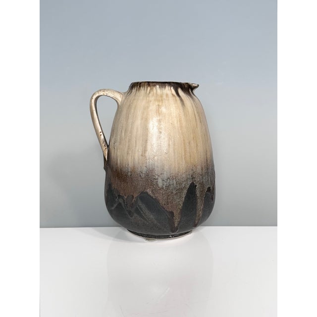 Handcrafted jug from a German studio ceramics workshop of the 1970s, featuring a naturally flowing beige-brown lava glaze...