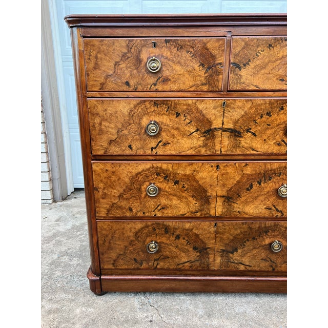 A handsome antique commode veneered in richly figured burr walnut, featuring four graduated drawers, molded edges, and...