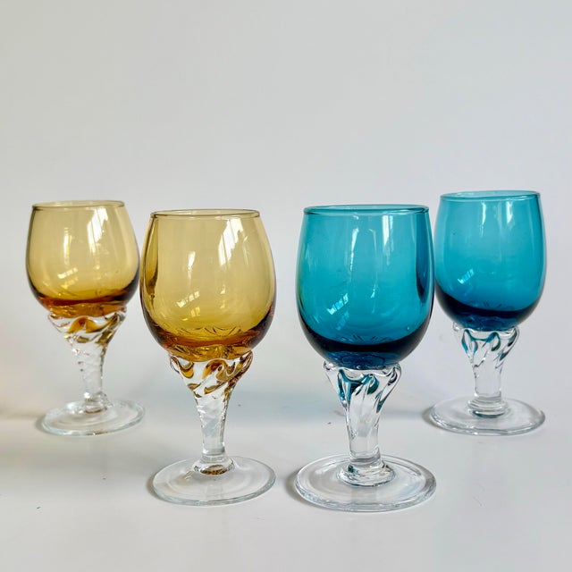 A charming set of four vintage cordial glasses featuring elegant twisted clear stems and jewel-toned bowls in peacock blue...