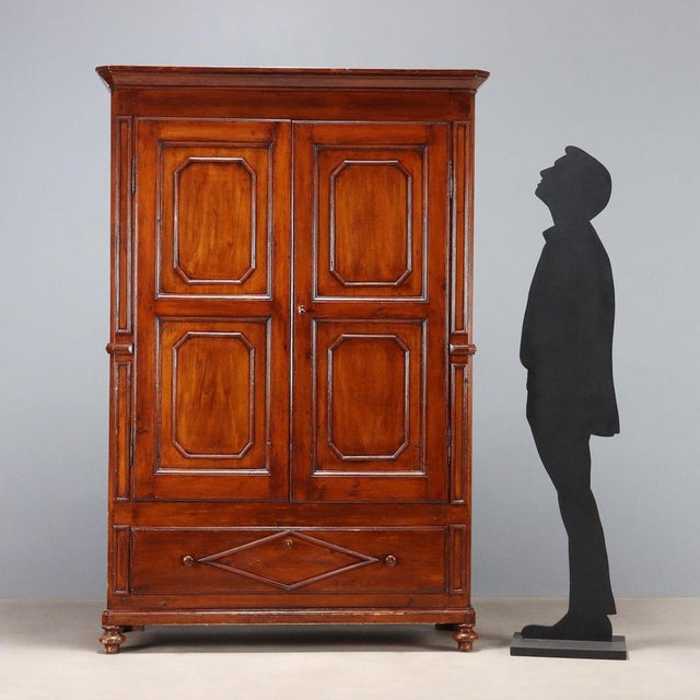 Double-piece wardrobe in walnut-stained poplar. Front with a pair of paneled doors and a drawer underneath, paneled sides,...