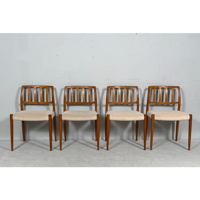 Construction made of varnished teak, each with vertically braced backrests and a padded seat upholstered in beige wool...