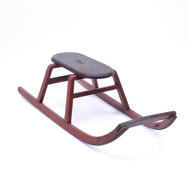 Wooden sled with metal runners under the rockers. The legs and rockers have the original red paint and the seat has its...