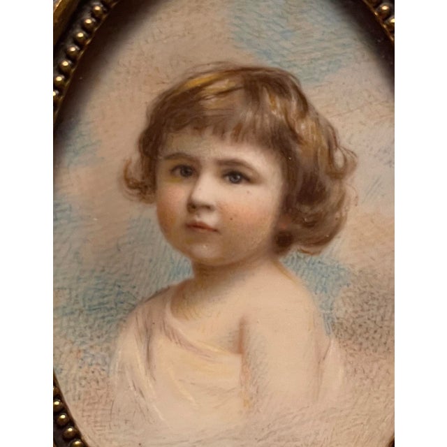 Antique portrait miniature of a small child, brass frame with a floral swag at the top. Unsigned, marked with the name of...