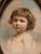 Antique portrait miniature of a small child, brass frame with a floral swag at the top. Unsigned, marked with the name of...