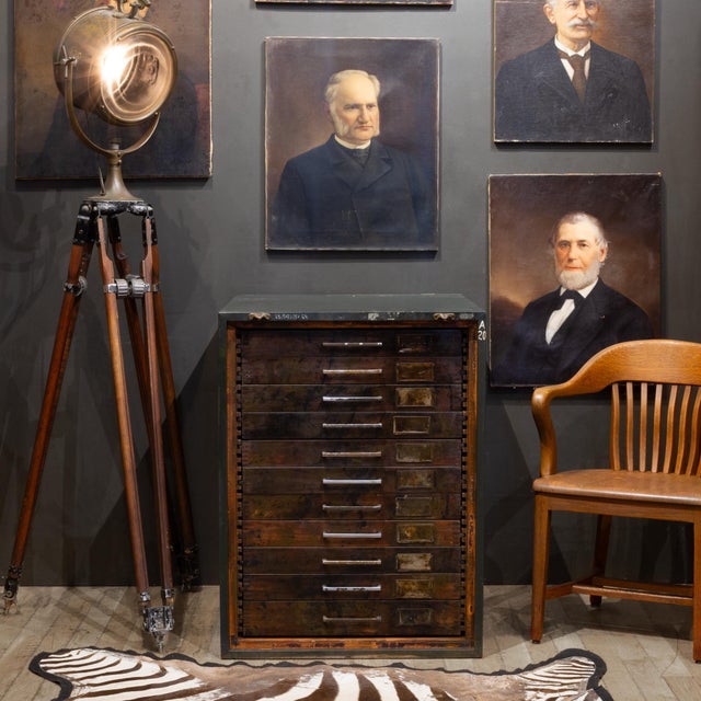 ABOUT An early 20th century flat file cabinet with eleven deep drawers, large metal pulls, two brass plated hooks and...