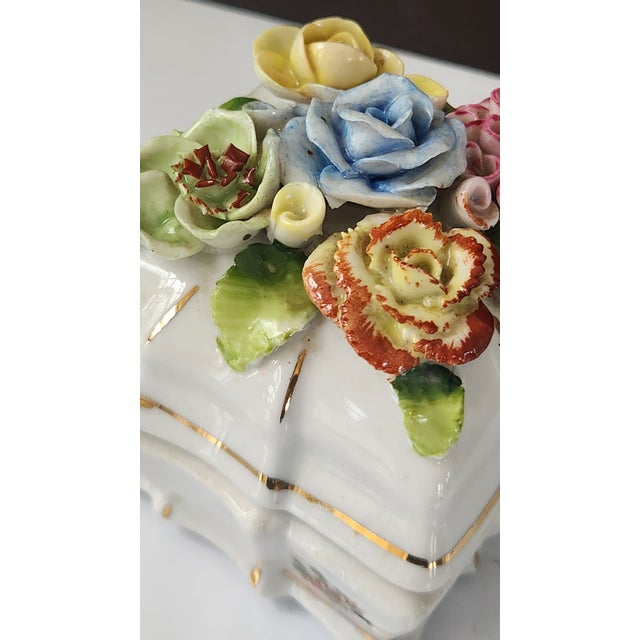 A mid-century European porcelain trinket box featuring a richly detailed lid with hand-applied porcelain flowers in pastel...