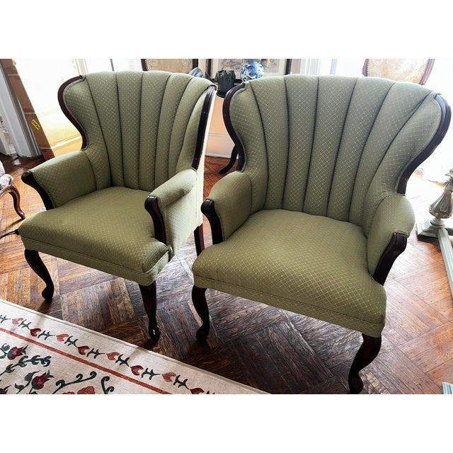 A striking pair of vintage wingback chairs in sage green upholstery with elegantly carved cabriole legs. The graceful...