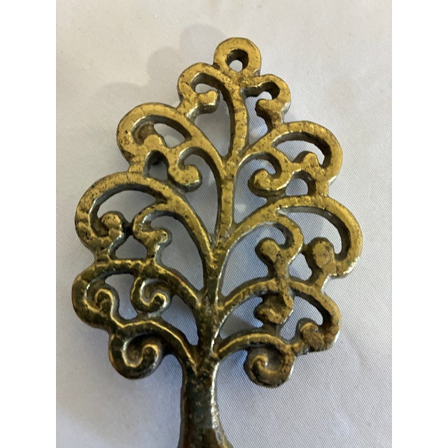 An ornate miniature tree-shaped trivet featuring open scrollwork branches and a warm brass-tone finish. this is a charming...