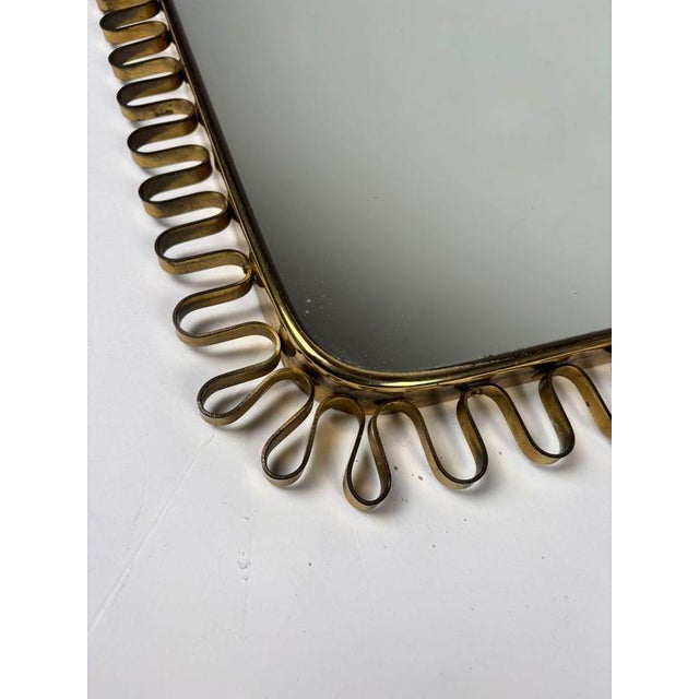 A mirror with a refined shape, inspired by the timeless style of Josef Frank, featuring a harmonious brass silhouette. The...