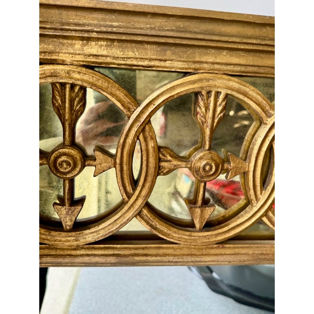 A sophisticated vintage neoclassical mirror featuring an architectural frieze of interlocking rings and classical arrow...
