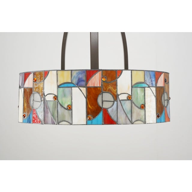 Mission style pendant light with an oval shaped drum shade. It is made of colorful stained glass in an abstract geometric...